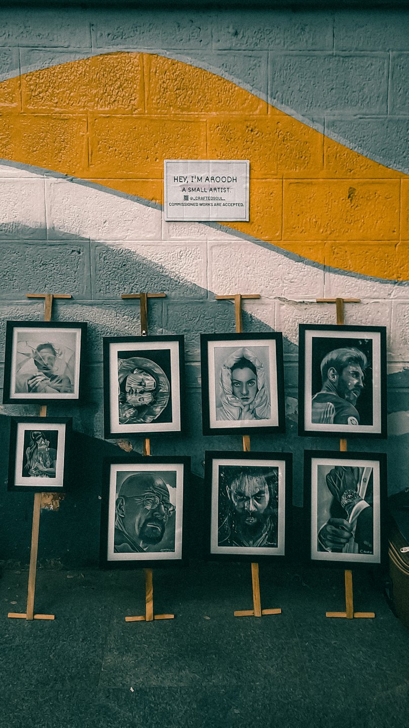 Pencil portraits on easels stand before a patterned brick wall.