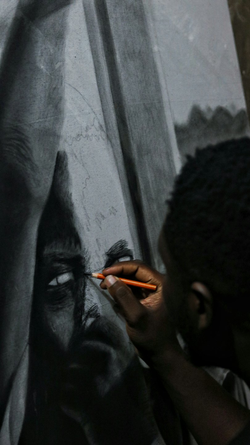 Artist's hand sketches an intense eye with an orange pencil.