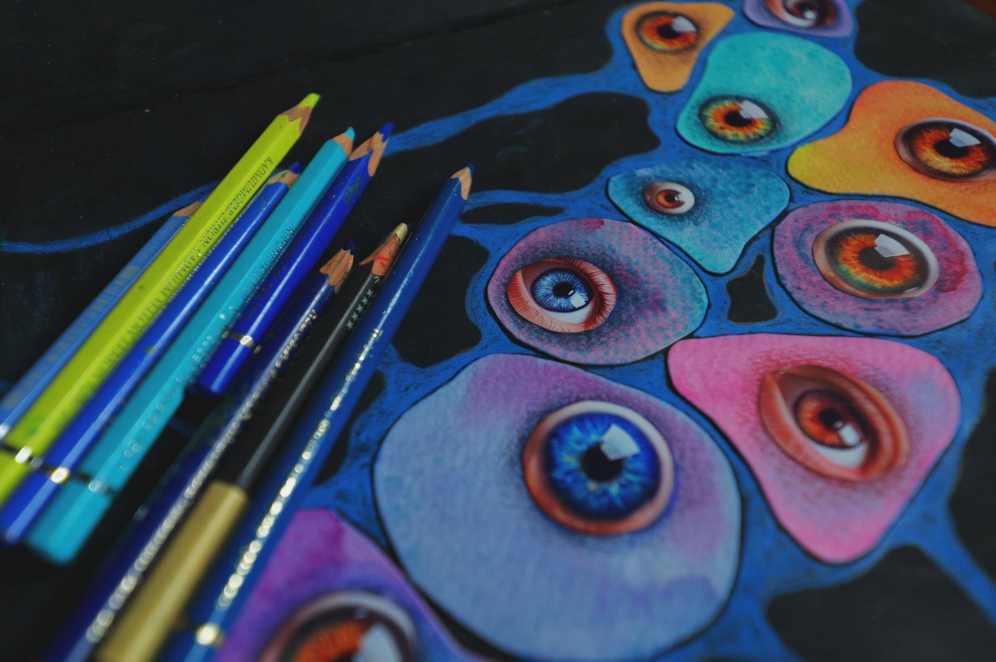 Colored pencils rest next to an abstract painting of eyes.